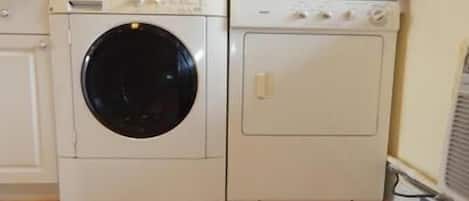 Un lavadero pequeño y blanco, con lavadora y secadora, suelo de madera y salpicadero de azulejos.