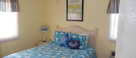 Un dormitorio con cama, mesita de noche, lámpara y un mapa enmarcado en la pared.