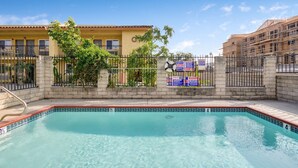 A swimming pool with a tiled edge, surrounded by a fence and a building with balconies.