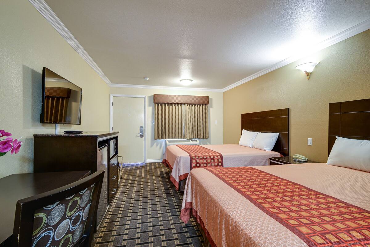 A hotel room with two beds, a desk, a chair, a television, and a bathroom with a shower curtain.