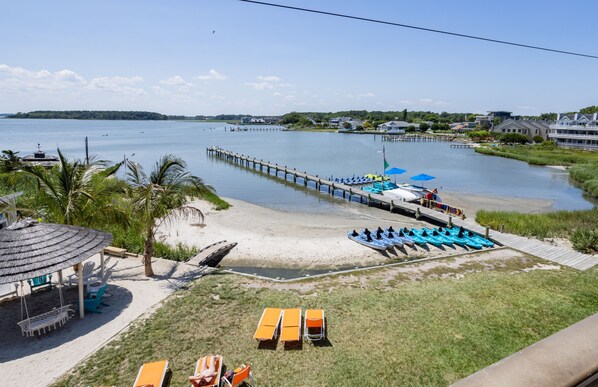 A beach with a dock, lounge chairs, and a thatched-roof structure.