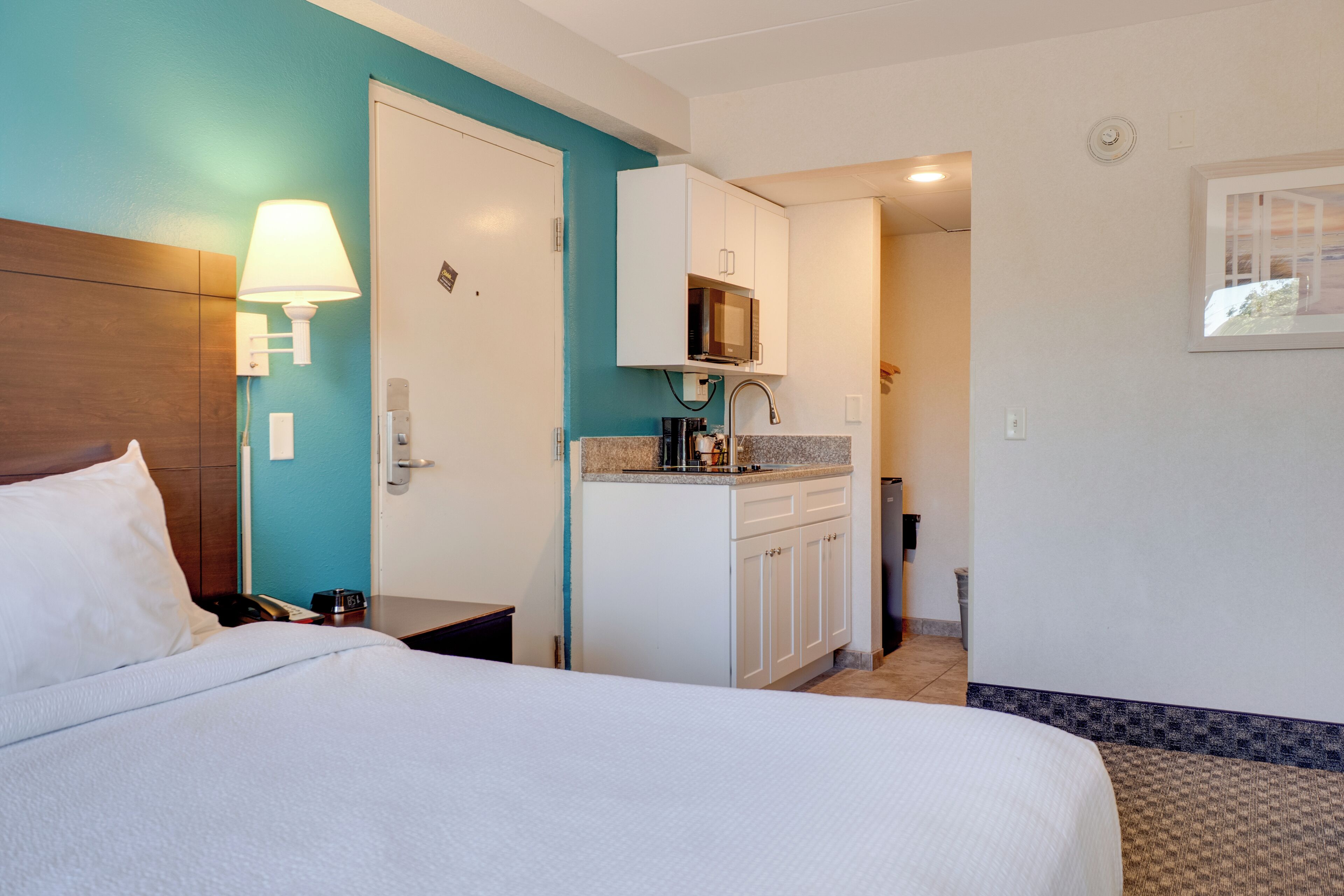Habitación de hotel con cama, escritorio, microondas y una pequeña kitchenette.