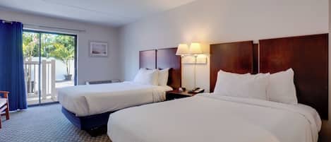 A hotel room with two beds, a desk, a chair, a lamp, and a view of the outdoors.