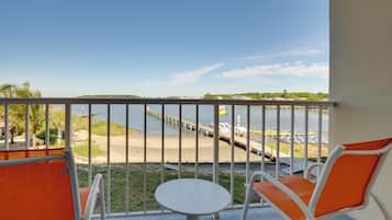 Un balcón con vista a un muelle y barcos, una mesa pequeña y sillas naranjas.