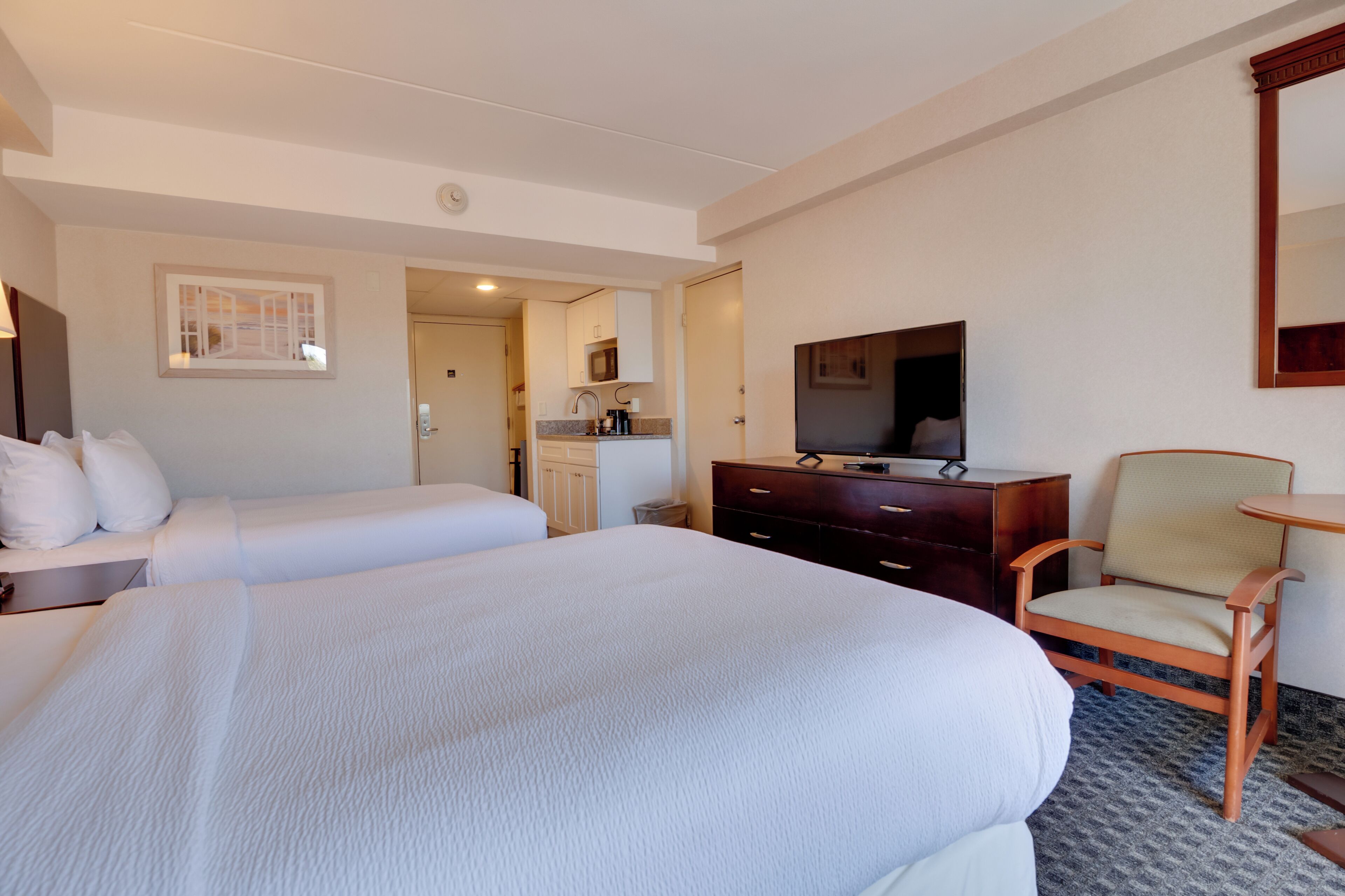 Habitación de hotel con dos camas, televisión, escritorio, silla y una pequeña kitchenette.