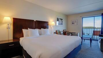 A hotel room with a large bed, bedside lamps, a desk, and a balcony with a view.