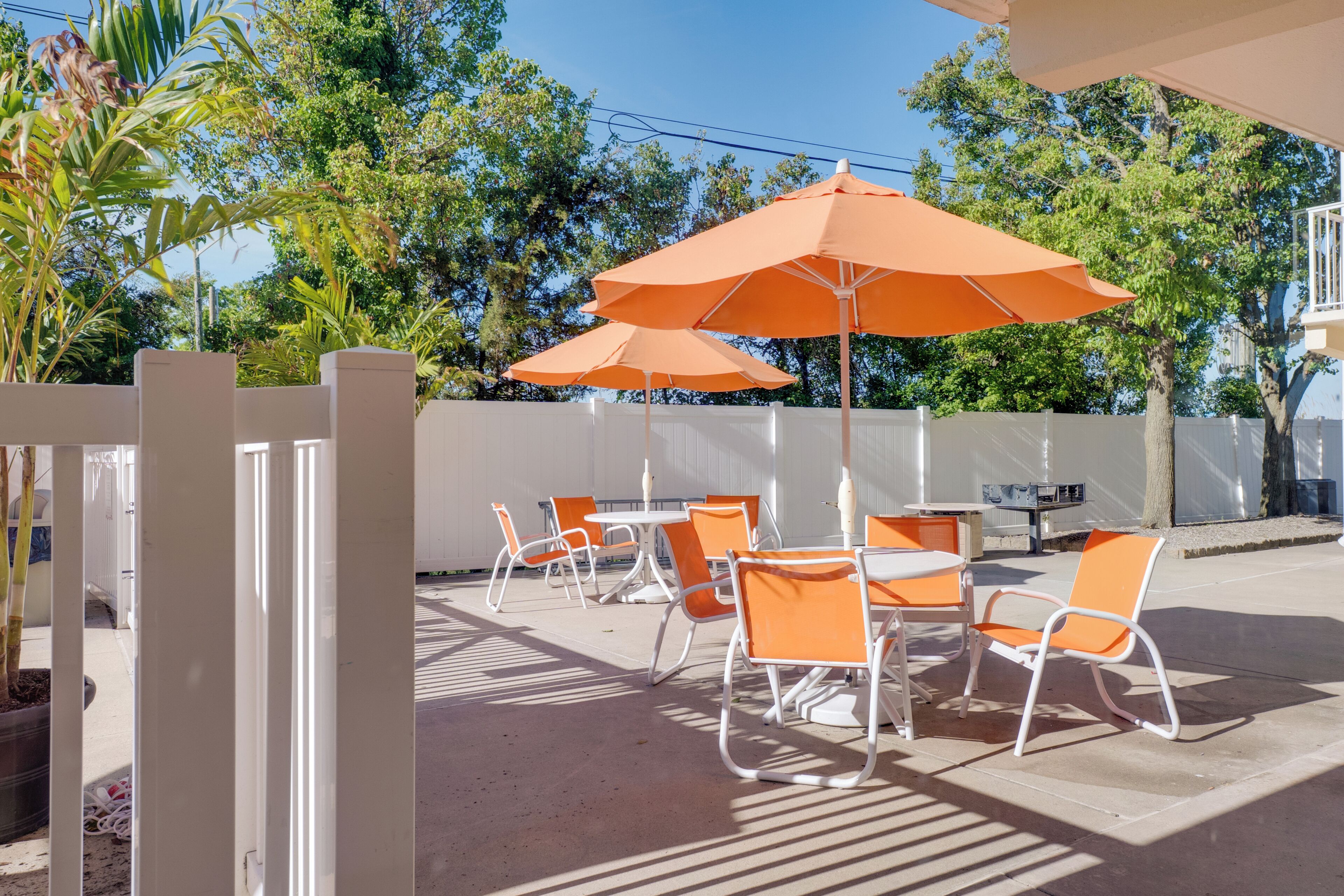 Outdoor seating with orange umbrellas, white chairs, and a white fence.