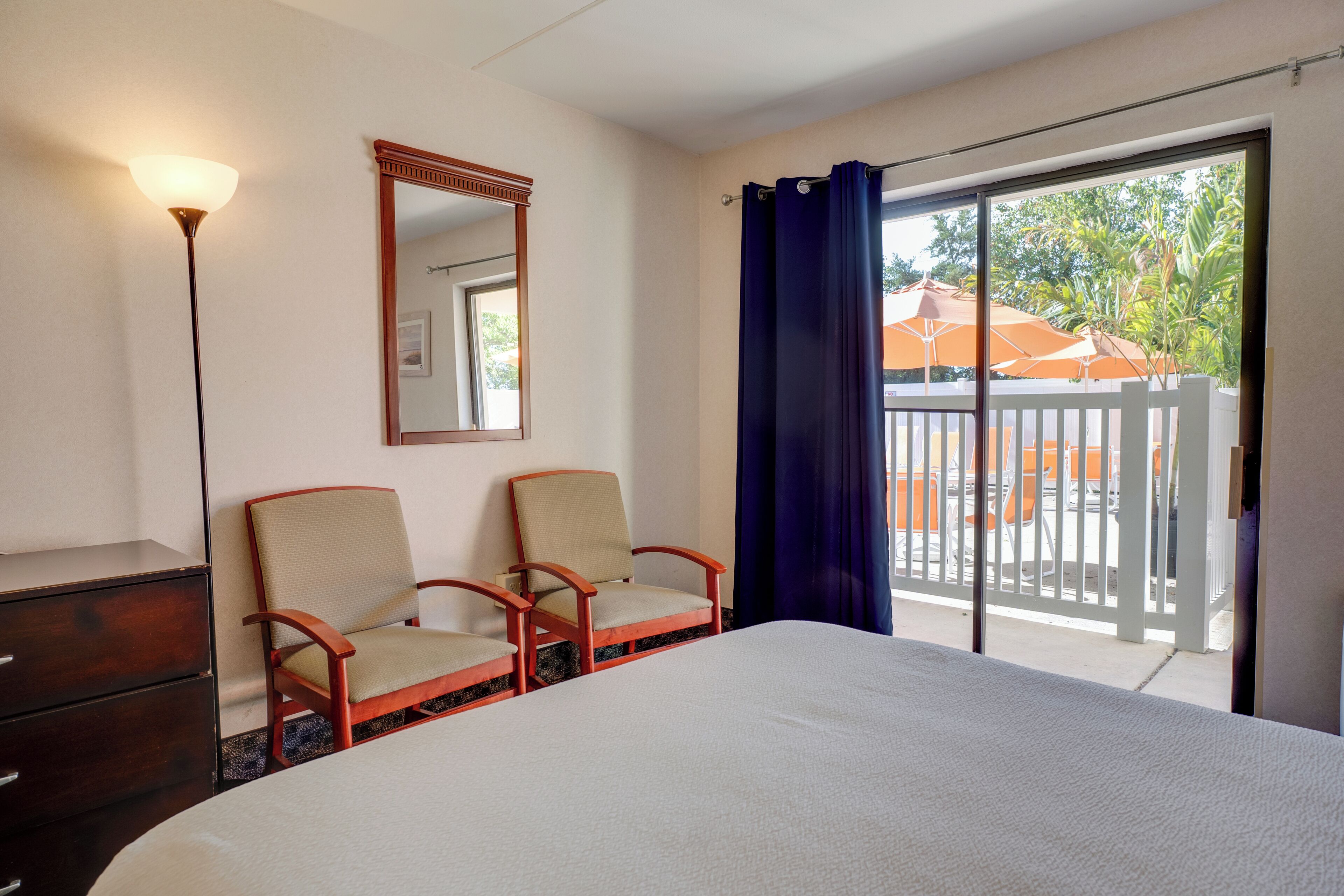 A hotel room with a bed, two chairs, a dresser, a mirror, and a balcony with a view of the outside.