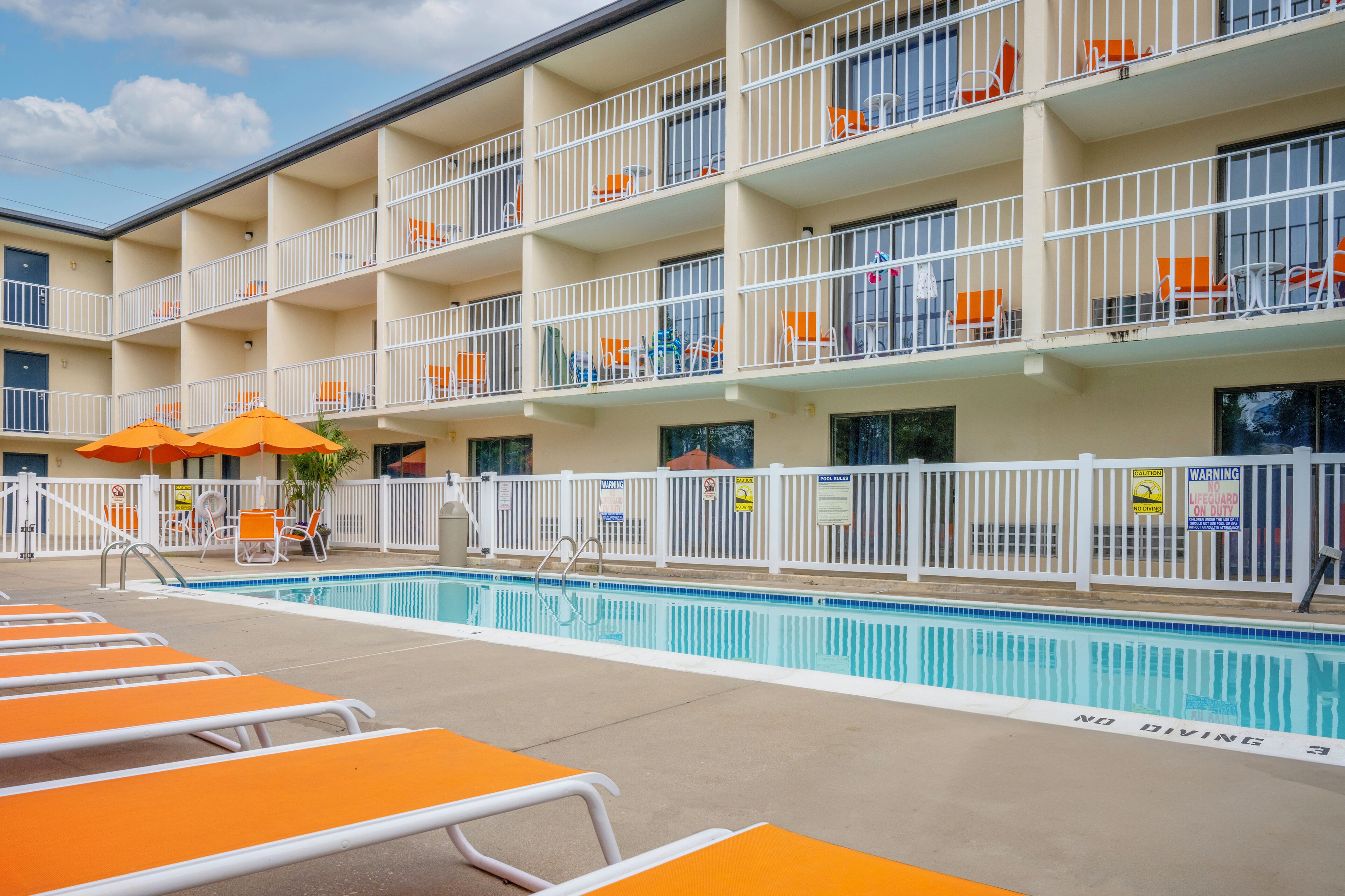Un hôtel à plusieurs étages doté d’une piscine, de chaises longues orange et de rampes blanches.