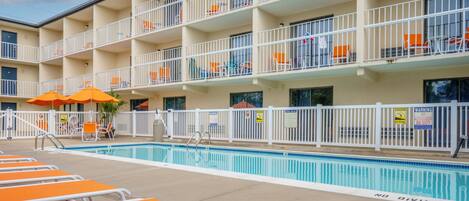 Un hôtel à plusieurs étages doté d’une piscine, de chaises longues orange et de rampes blanches.