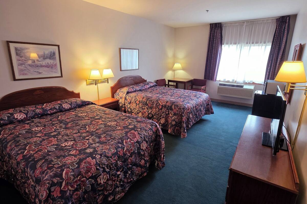 Une chambre d’hôtel avec deux lits, un bureau, une chaise et une fenêtre avec des rideaux.