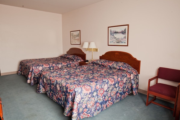 A hotel room with two beds, a wooden headboard, a chair, and two wall-mounted lamps.