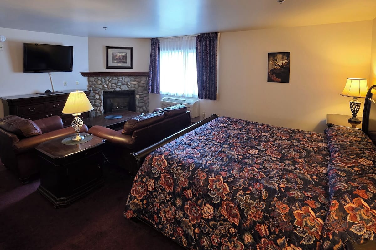 Une chambre d’hôtel avec un grand lit, un canapé, une télévision, une cheminée et une lampe.