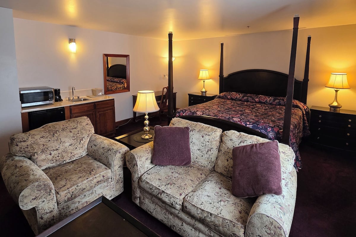 Une chambre d’hôtel avec un lit à baldaquin, deux canapés à motifs floraux, une machine à café, une lampe et une petite table.