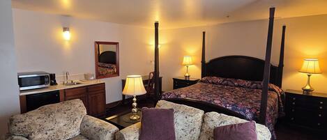 A hotel room with a four-poster bed, two floral-patterned sofas, a coffee machine, a lamp, and a small table.