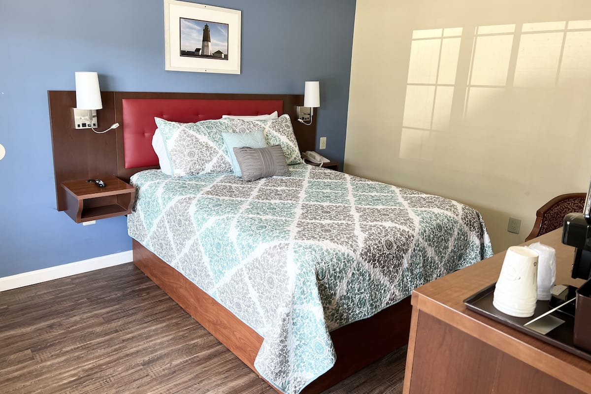 Habitación de hotel ordenada, con cama, lámparas de noche, mesita de noche, un cuadro en la pared y un escritorio de madera con lámpara.