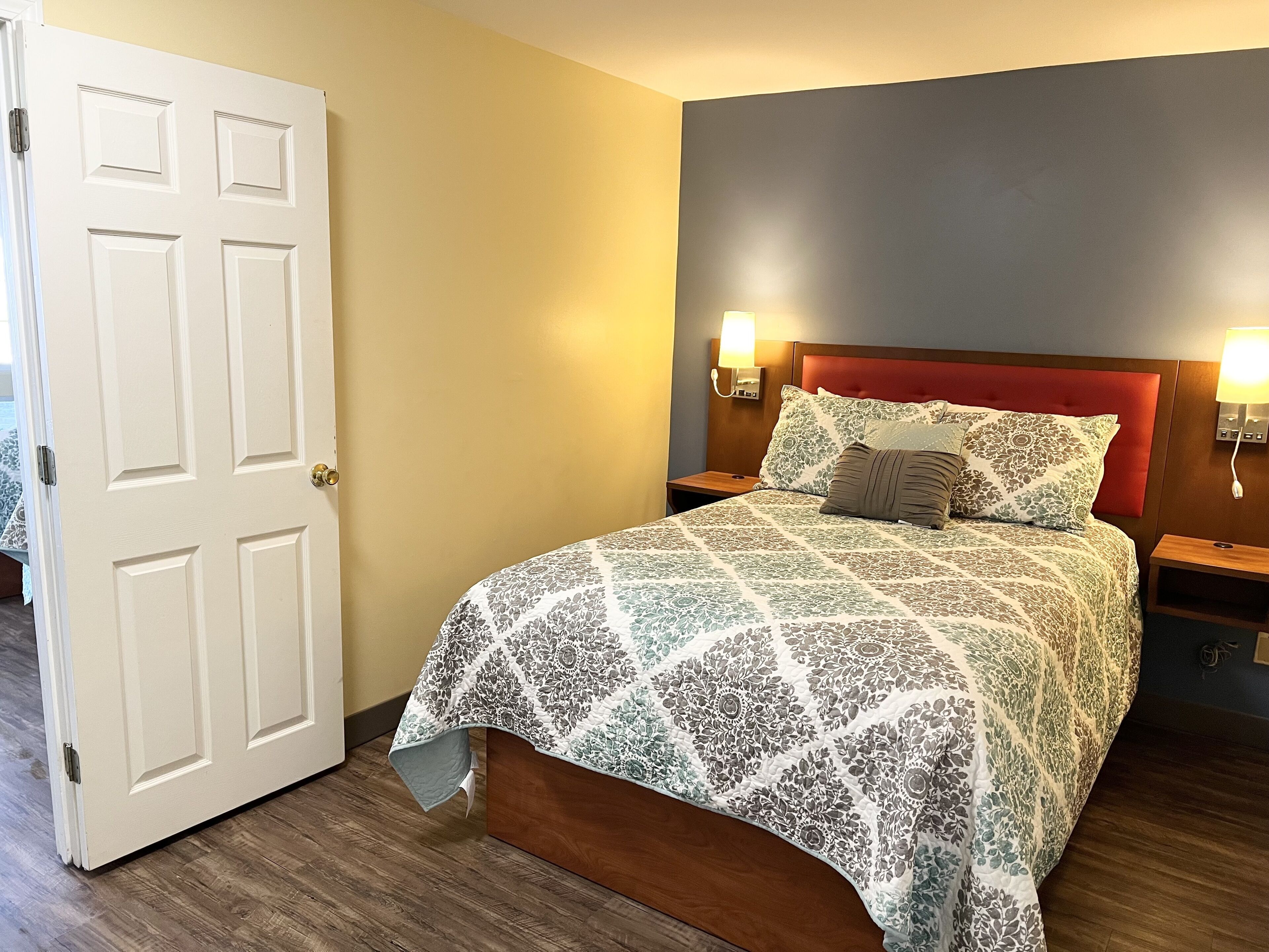 A neatly made bed with a floral-patterned bedspread, two bedside lamps, and a wooden nightstand.
