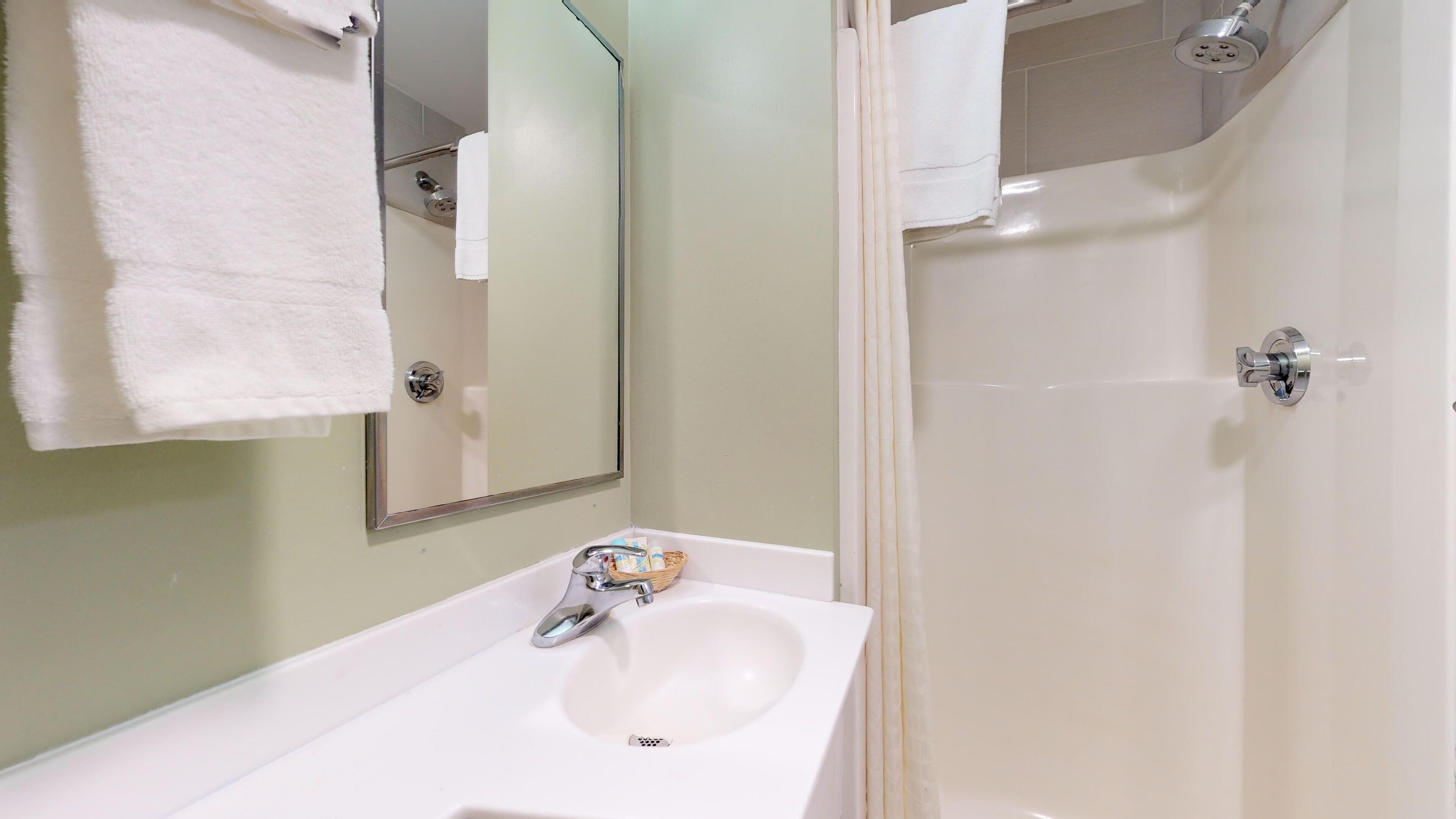 Un baño con lavamanos blanco, espejo y zona de ducha.