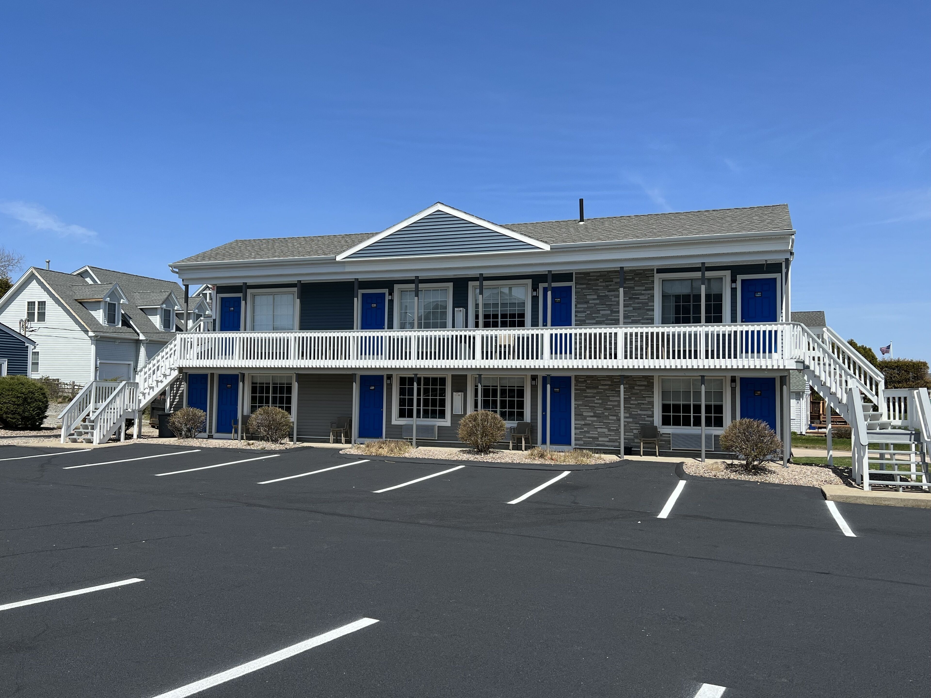 Un motel à deux étages doté d’un balcon central, d’un parking et surplombant un ciel d’un bleu limpide.