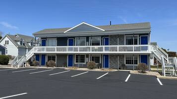 A two-story motel with a central balcony, a parking lot, and a clear blue sky.