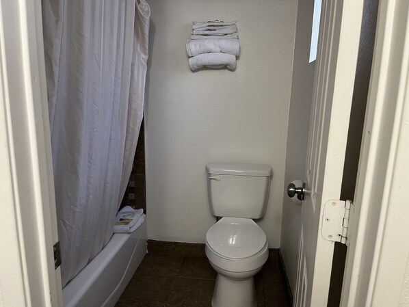 Une petite salle de bain avec des toilettes, un rideau de douche et une pile de serviettes accrochées au mur.