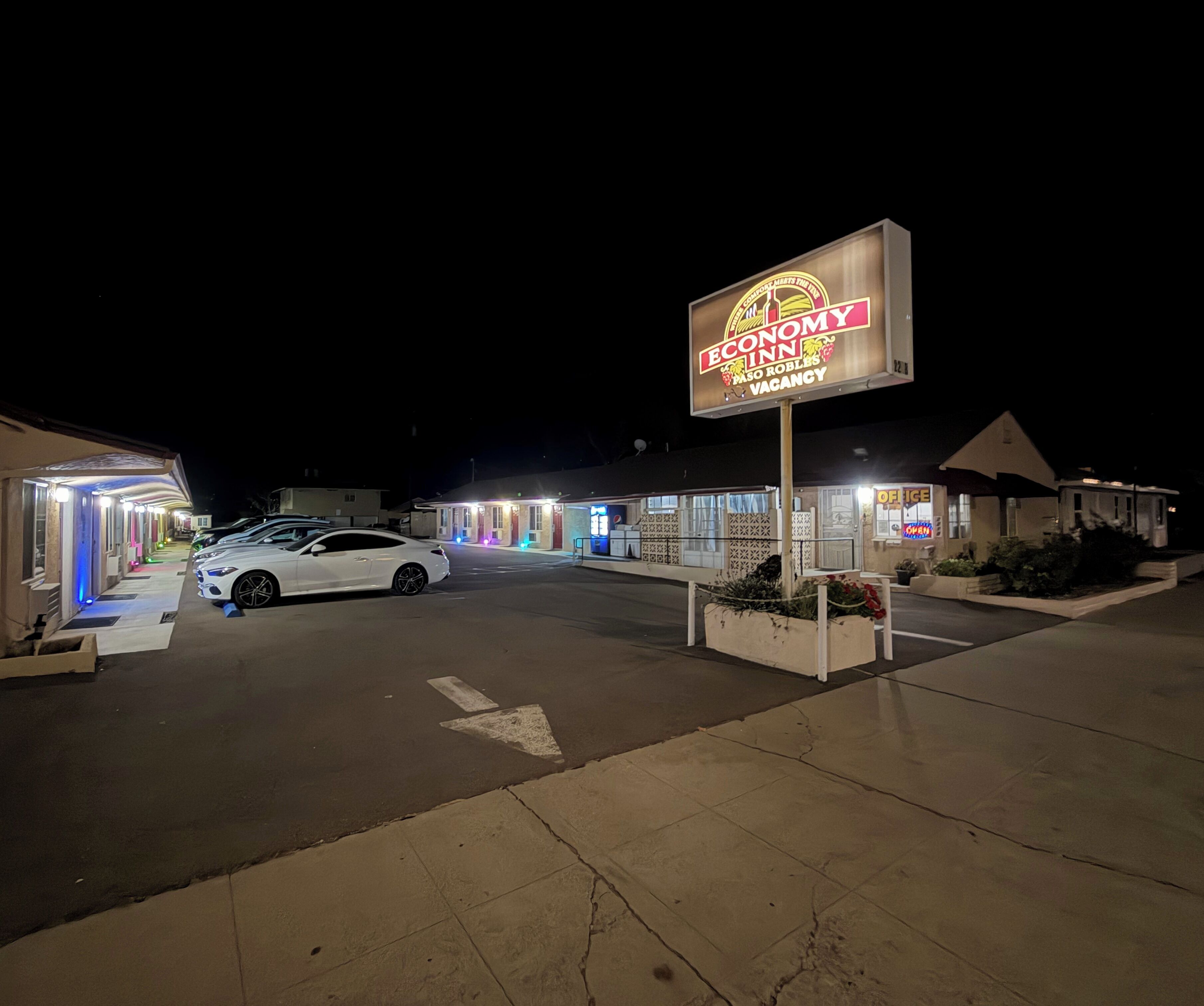 Un motel con un letrero de neón, un estacionamiento y un coche blanco estacionado al frente.