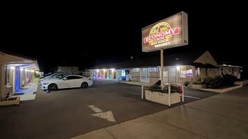 Un motel con un letrero de neón, un estacionamiento y un coche blanco estacionado al frente.