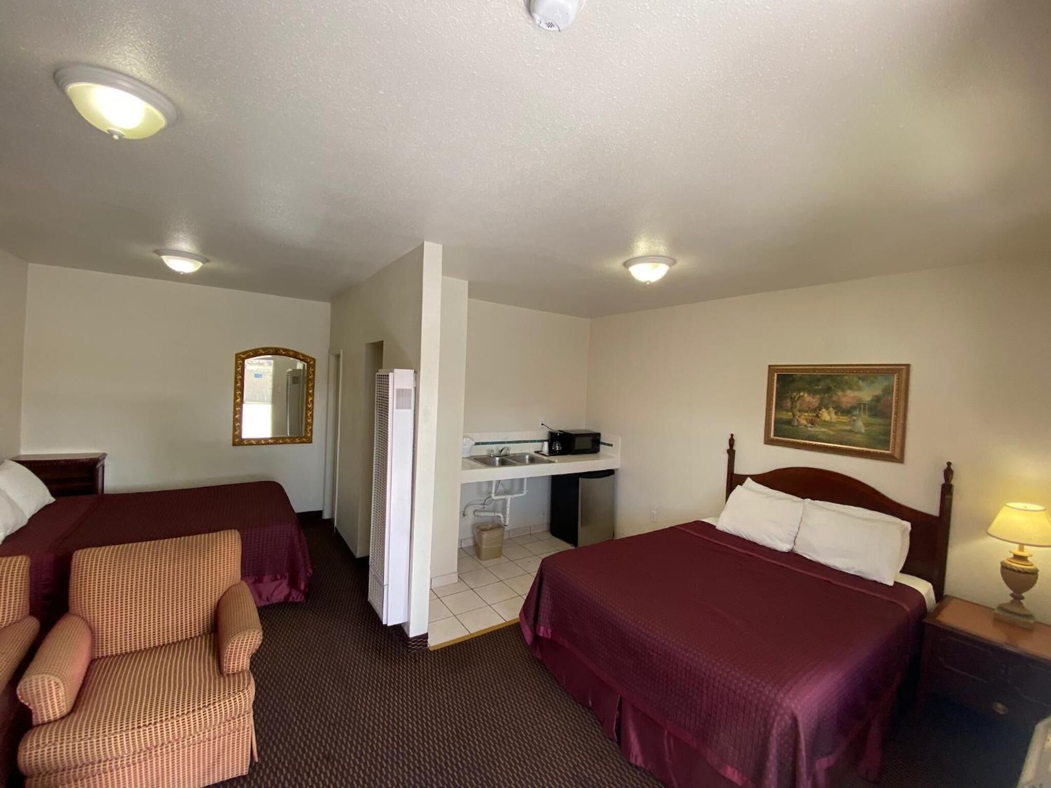 A hotel room with two beds, a desk, a chair, a mirror, and a painting on the wall.