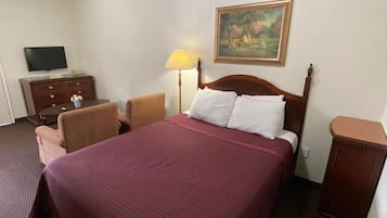 Un cuarto de hotel con una cama grande, un televisor en un tocador, una lámpara y un cuadro en la pared.