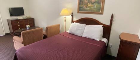 Une chambre d’hôtel avec un grand lit, un téléviseur posé sur une commode, une lampe et un tableau au mur.