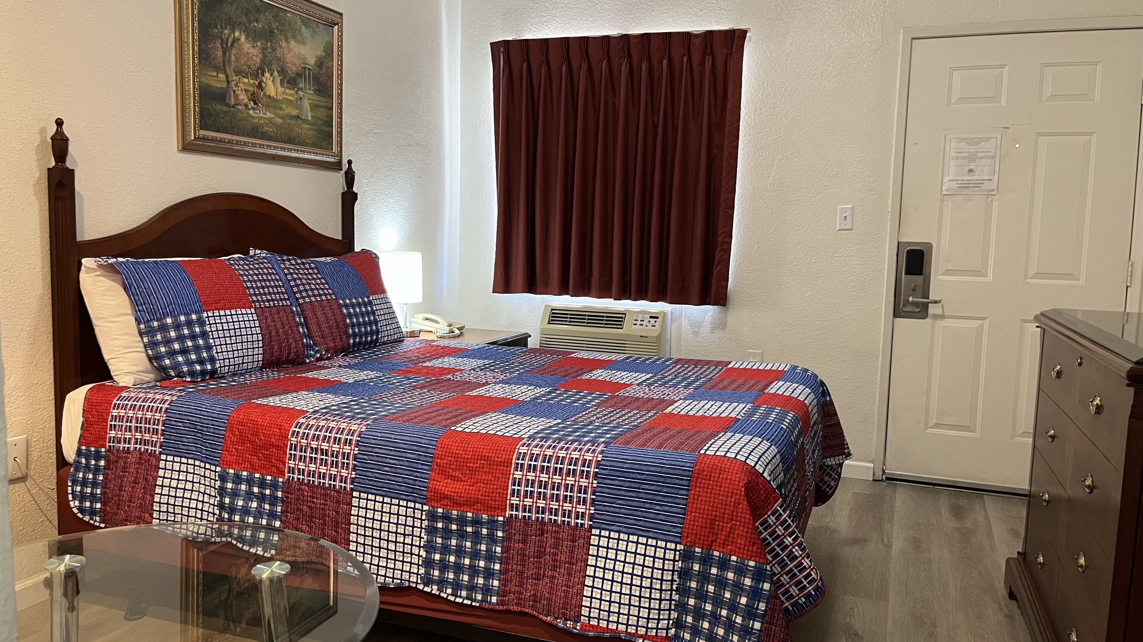 Quarto com cama, mesa de cabeceira, luminária, janela com cortinas, porta e cômoda.