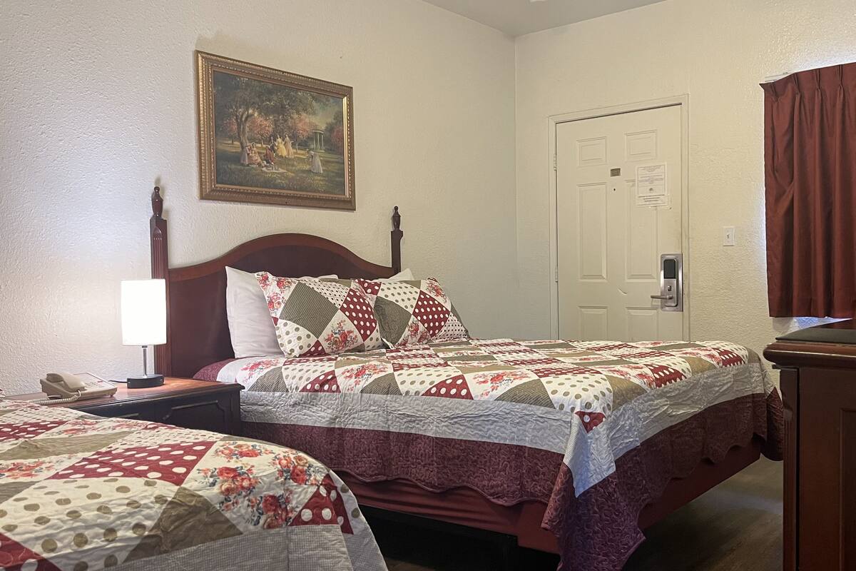 A hotel room with two beds, a painting on the wall, a door with a lock, and a window with curtains.