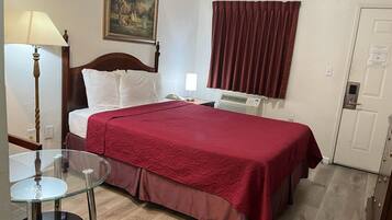 Une chambre d’hôtel avec un lit, une table en verre, une lampe, un tableau, une fenêtre avec des rideaux et une porte.