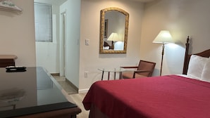 Ein Hotelzimmer mit einem Bett, einem Schreibtisch, einem Sessel, einem kleinen Tisch, einem Spiegel und zwei Lampen.