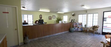 A reception area with a wooden counter, a computer, framed pictures, and a potted plant.
