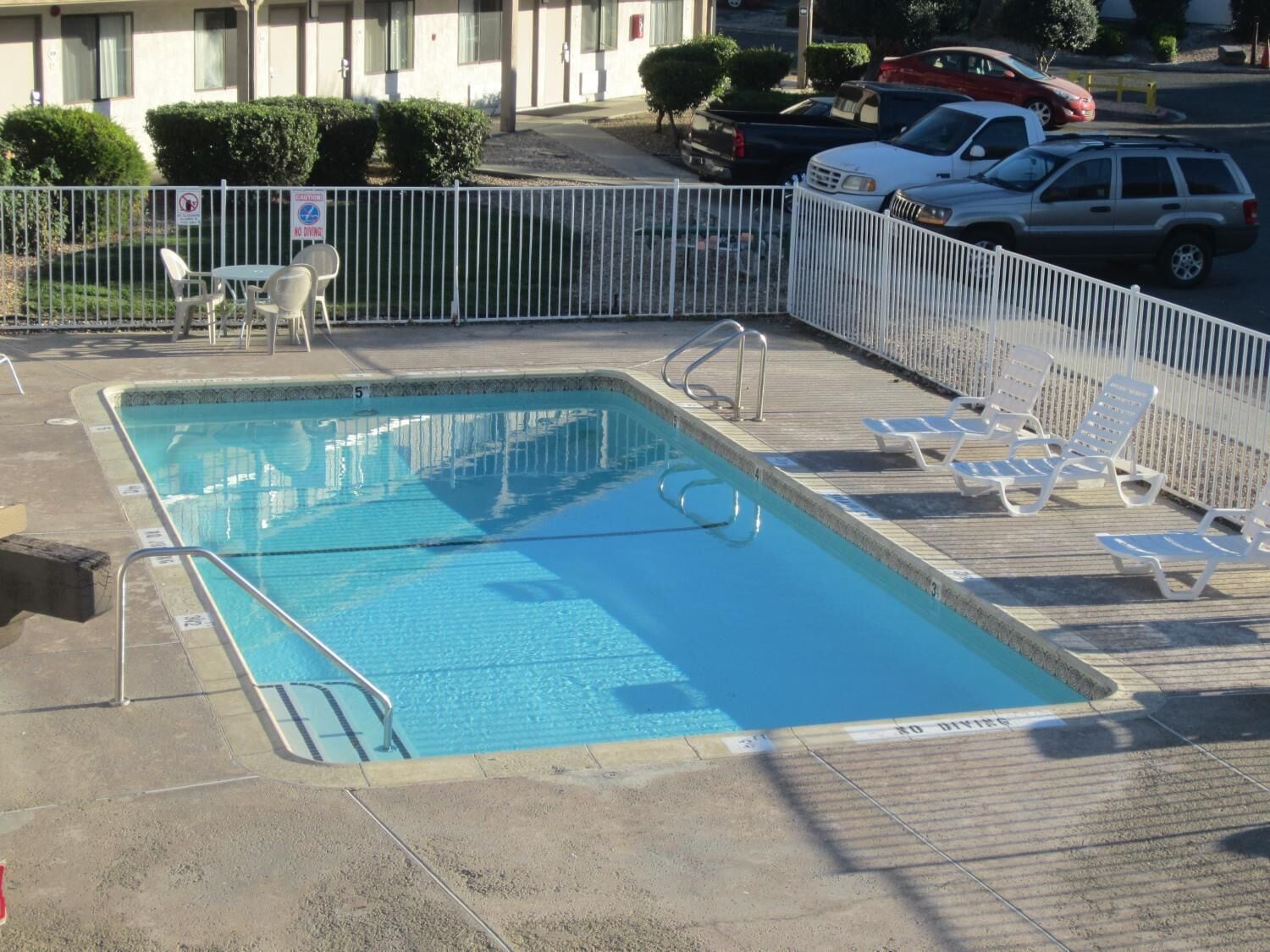 Une piscine rectangulaire entourée d’une clôture blanche et agrémentée de chaises longues.