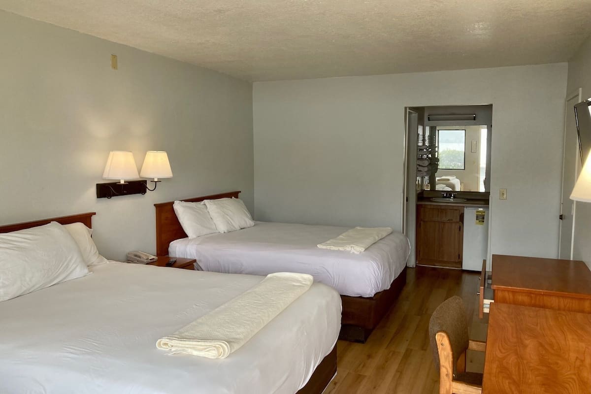 A hotel room with two beds, a desk, and a kitchenette.