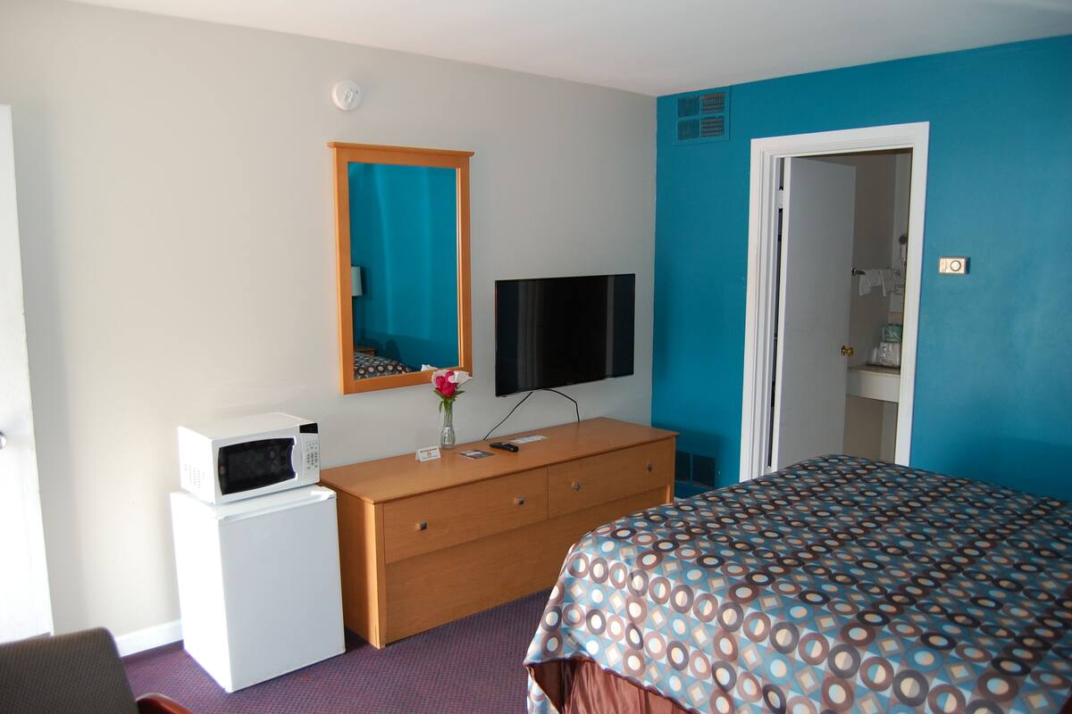 A hotel room with a bed, a dresser, a microwave, a TV, and a door leading to a bathroom.
