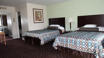 A hotel room with two beds, a desk, and a chair. There is a framed picture on the wall and a lamp on the nightstand.