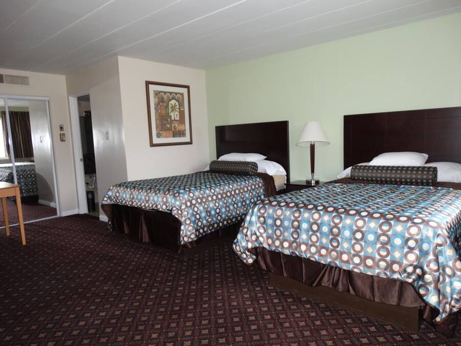 A hotel room with two beds, a desk, and a chair. There is a framed picture on the wall and a lamp on the nightstand.