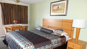 A hotel room with a bed, a desk, a chair, a nightstand, a lamp, and a painting on the wall.