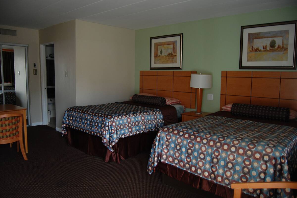 A hotel room with two beds, a desk, and a chair. There are two paintings on the walls.