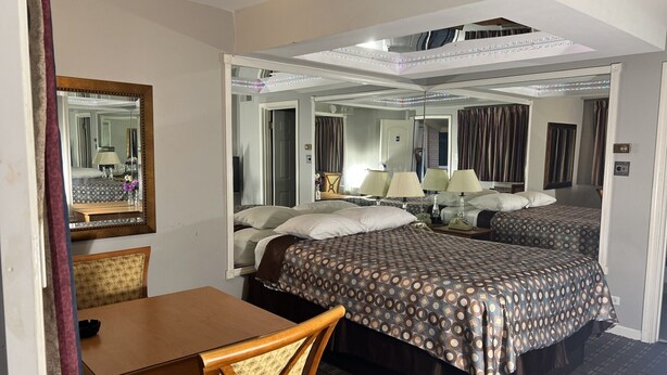 A hotel room with two beds, a wooden table, a chair, and a large mirror.