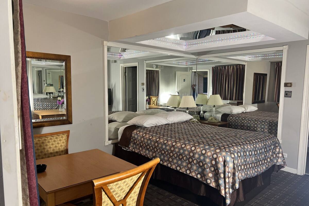 A hotel room with two beds, a wooden table, a chair, and a large mirror.