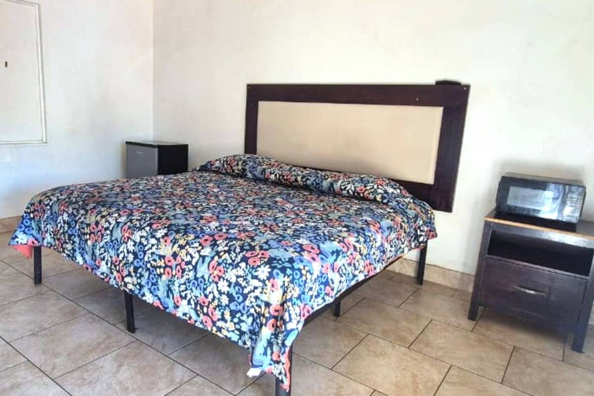 A bed with a floral bedspread, a wooden headboard, a small bedside table with a television, and a cabinet.