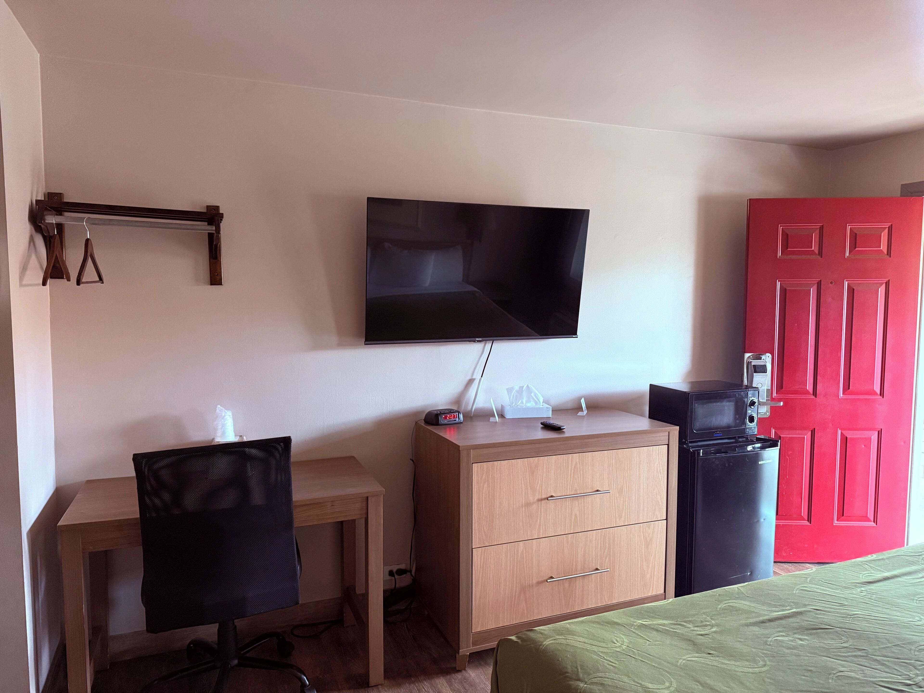 A room with a desk, chair, dresser, television, and a red door.