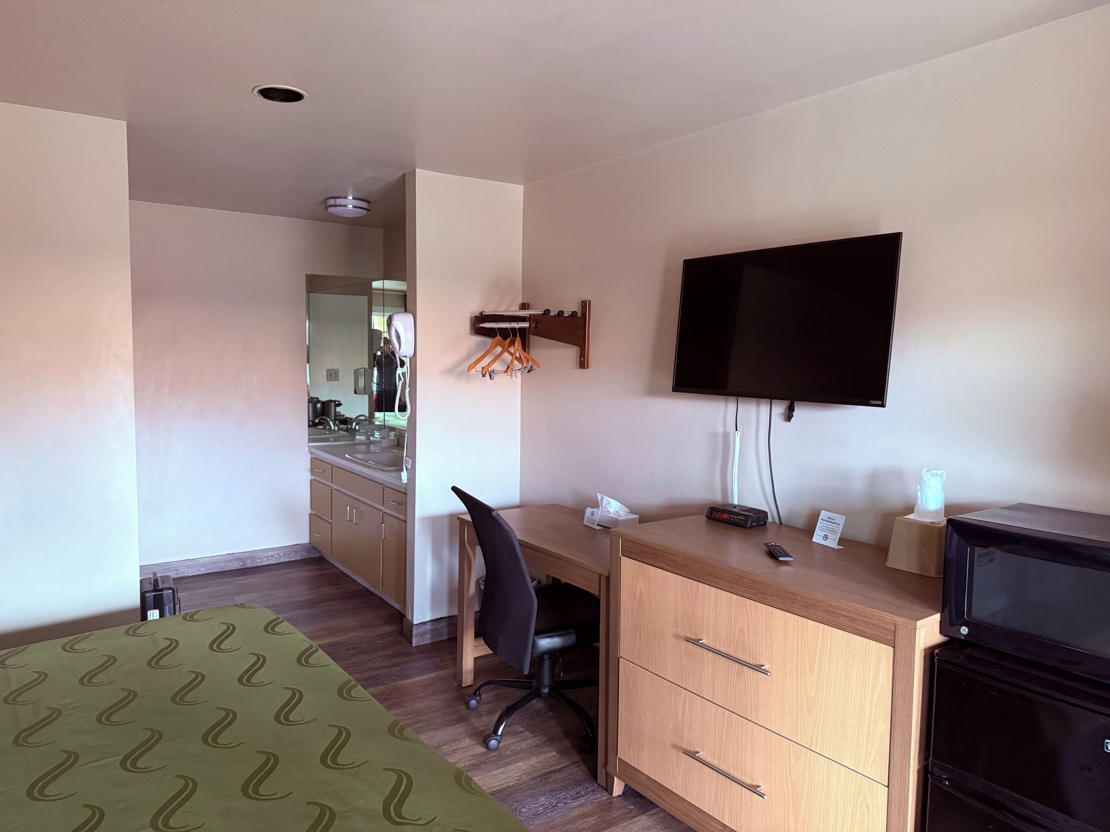 Una habitación de hotel con una cama, un escritorio con silla, televisor, cómoda y espejo.