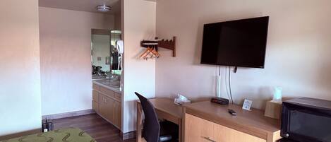 A hotel room with a bed, a desk with a chair, a television, a dresser, and a mirror.