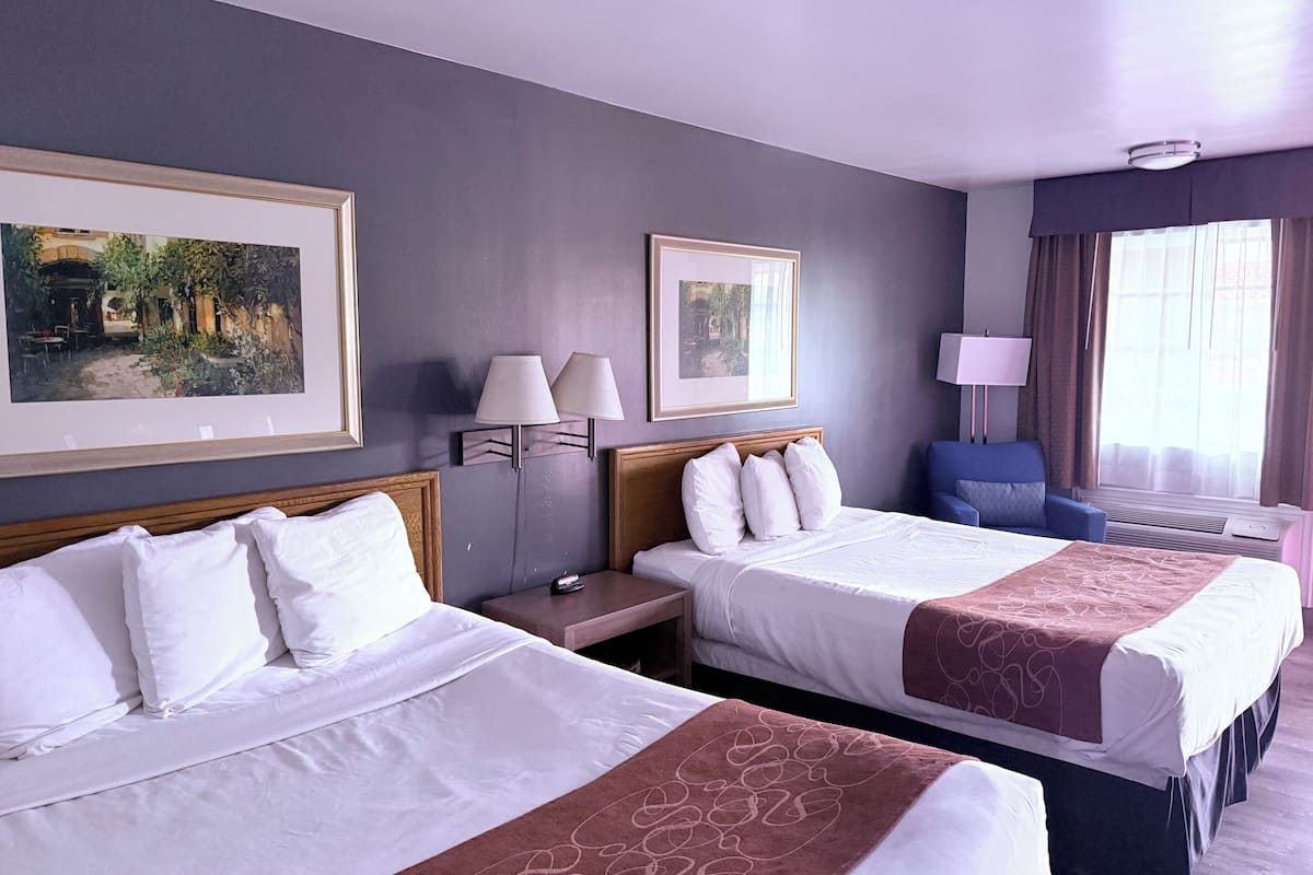 Quarto de hotel com duas camas, uma escrivaninha, uma cadeira e duas luminárias fixadas na parede.