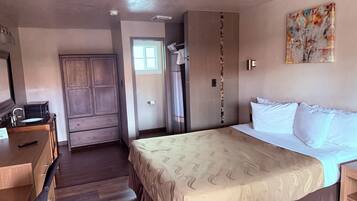 Habitación de hotel con cama, escritorio con lavabo, armario y un cuadro en la pared.